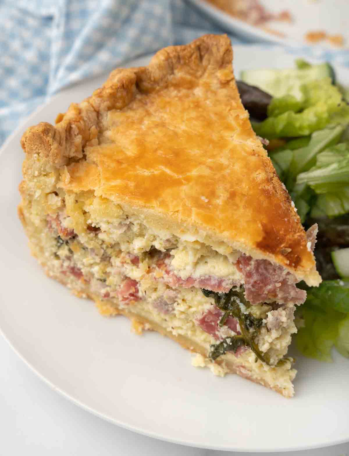 Slice of Pizza Rustica (Italian Easter Pie) on a white plate with salad.