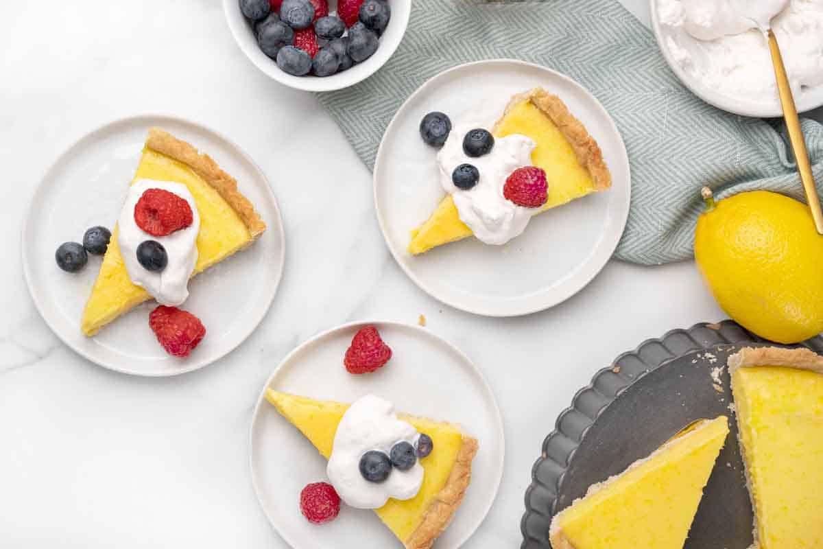 slices of lemon tart with whipped cream and berries on a white plates.