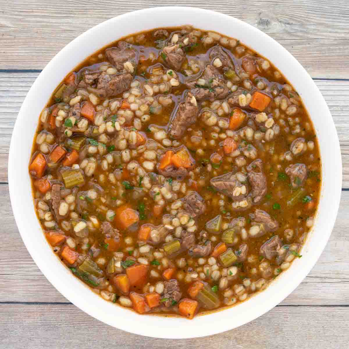 Beef barley soup in white bowl.