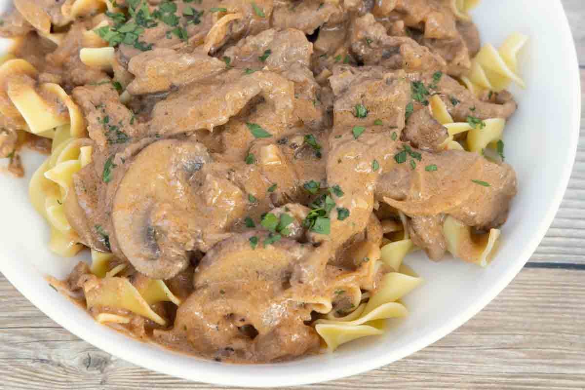 Beef stroganoff over egg noodles in white bowl.