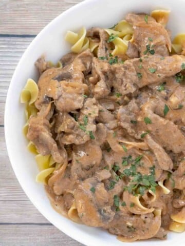 Beef stroganoff over egg noodles in white bowl.