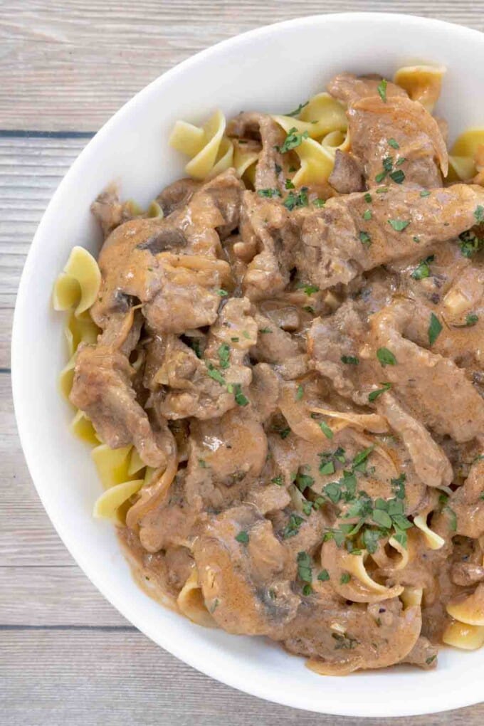 Beef stroganoff over egg noodles in white bowl.