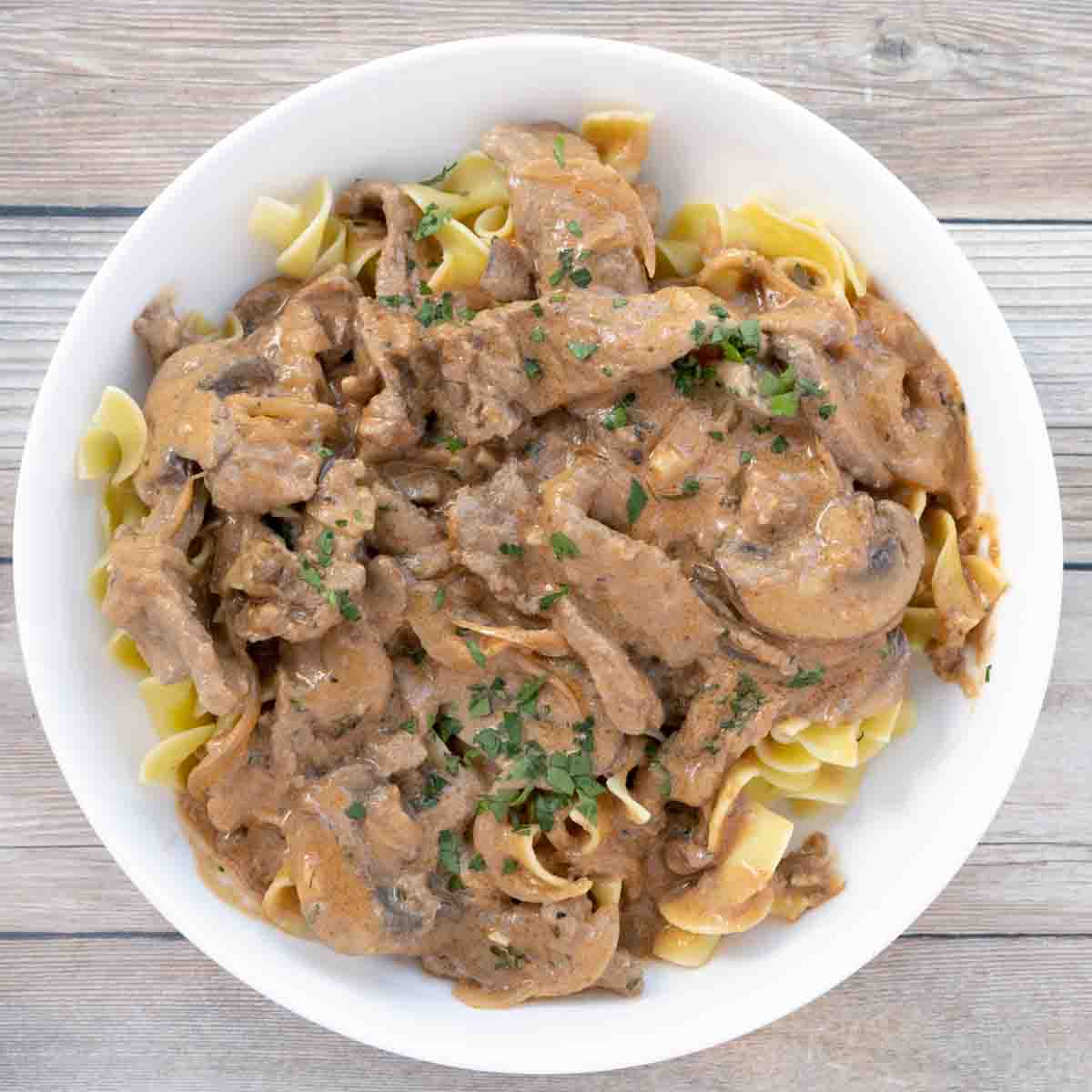 Beef stroganoff over egg noodles in white bowl.