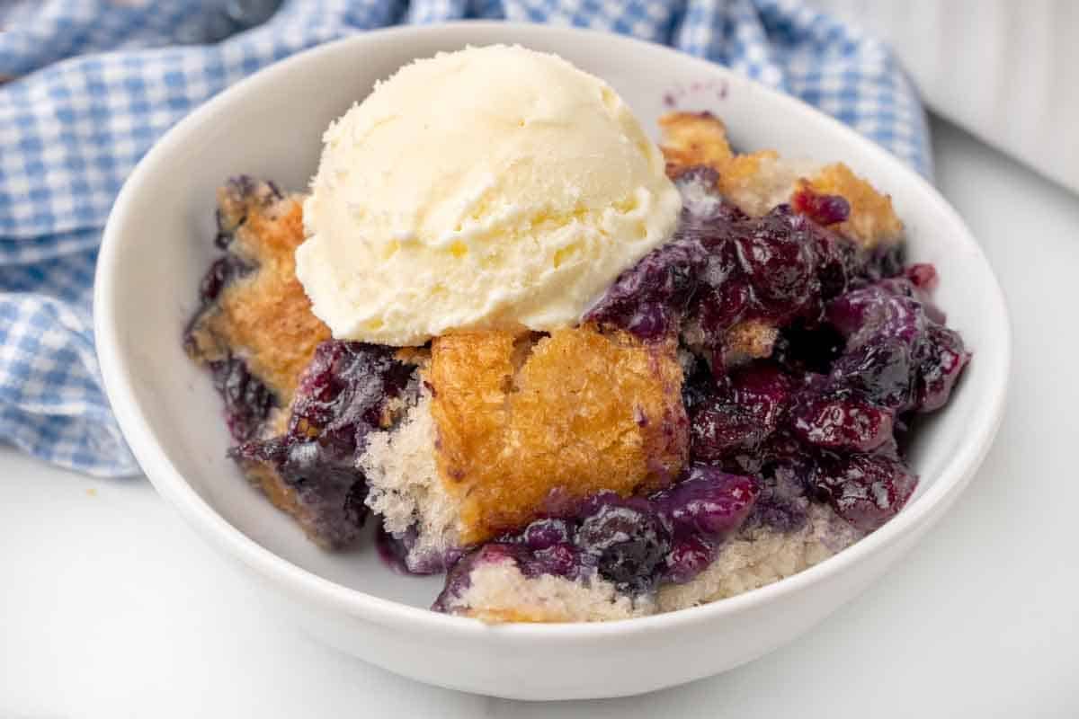 Blueberry cobbler with vanilla ice cream in a white bowl.