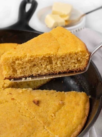 Slice of cornbread being taken out of the skillet.