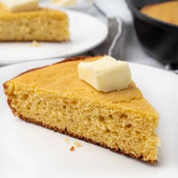 slice of skillet cornbread with pat of butter on a white plate.