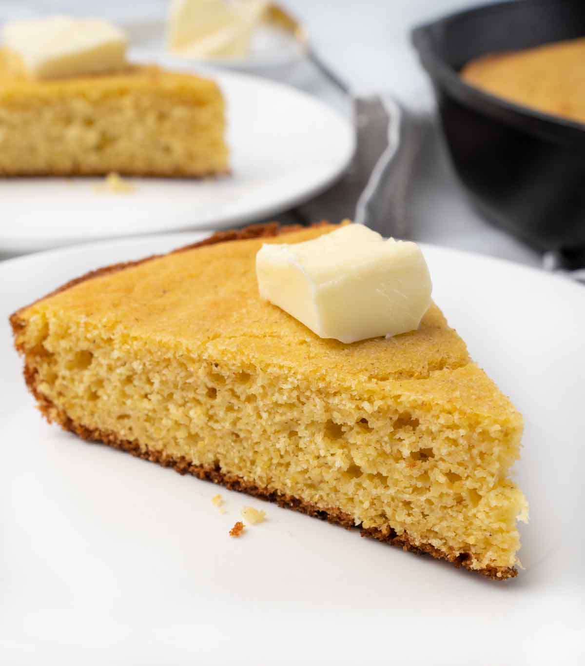slice of skillet cornbread with pat of butter on a white plate.