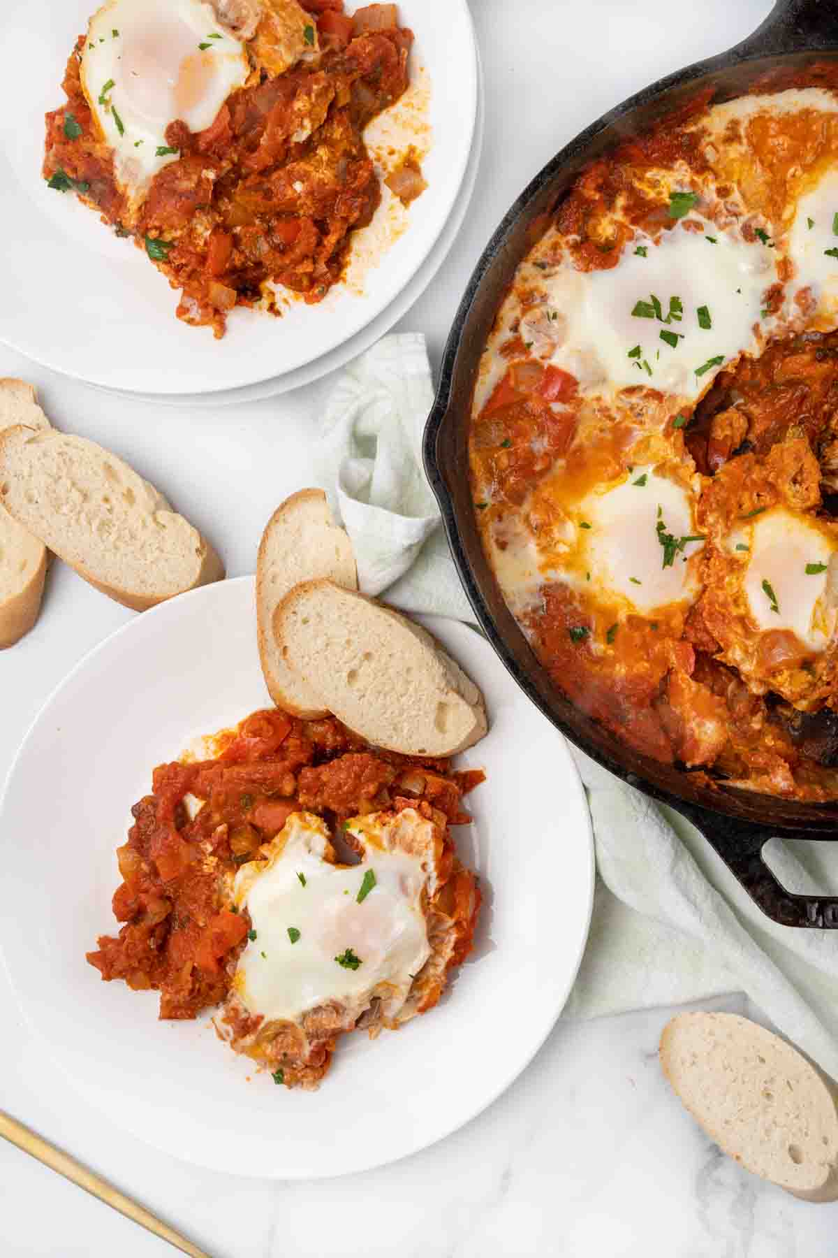 eggs in purgatory in a cast iron skillet with two servings on white plates.