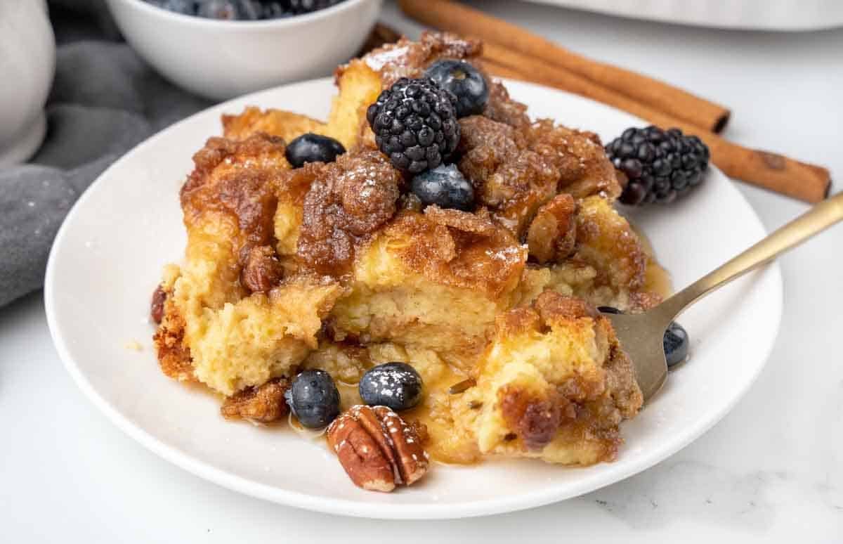 slice of french toast casserole with berries and syrup on white plate.