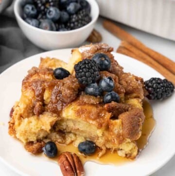 slice of french toast casserole with berries and syrup on white plate.