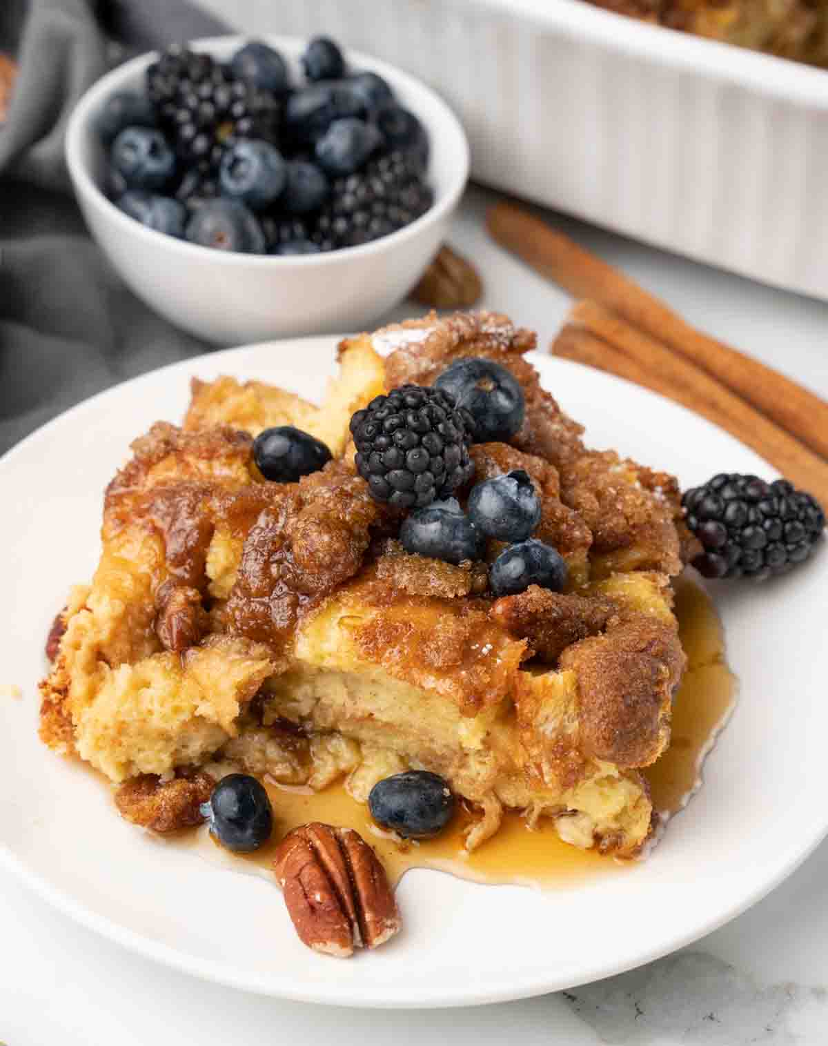 slice of french toast casserole with berries and syrup on white plate.