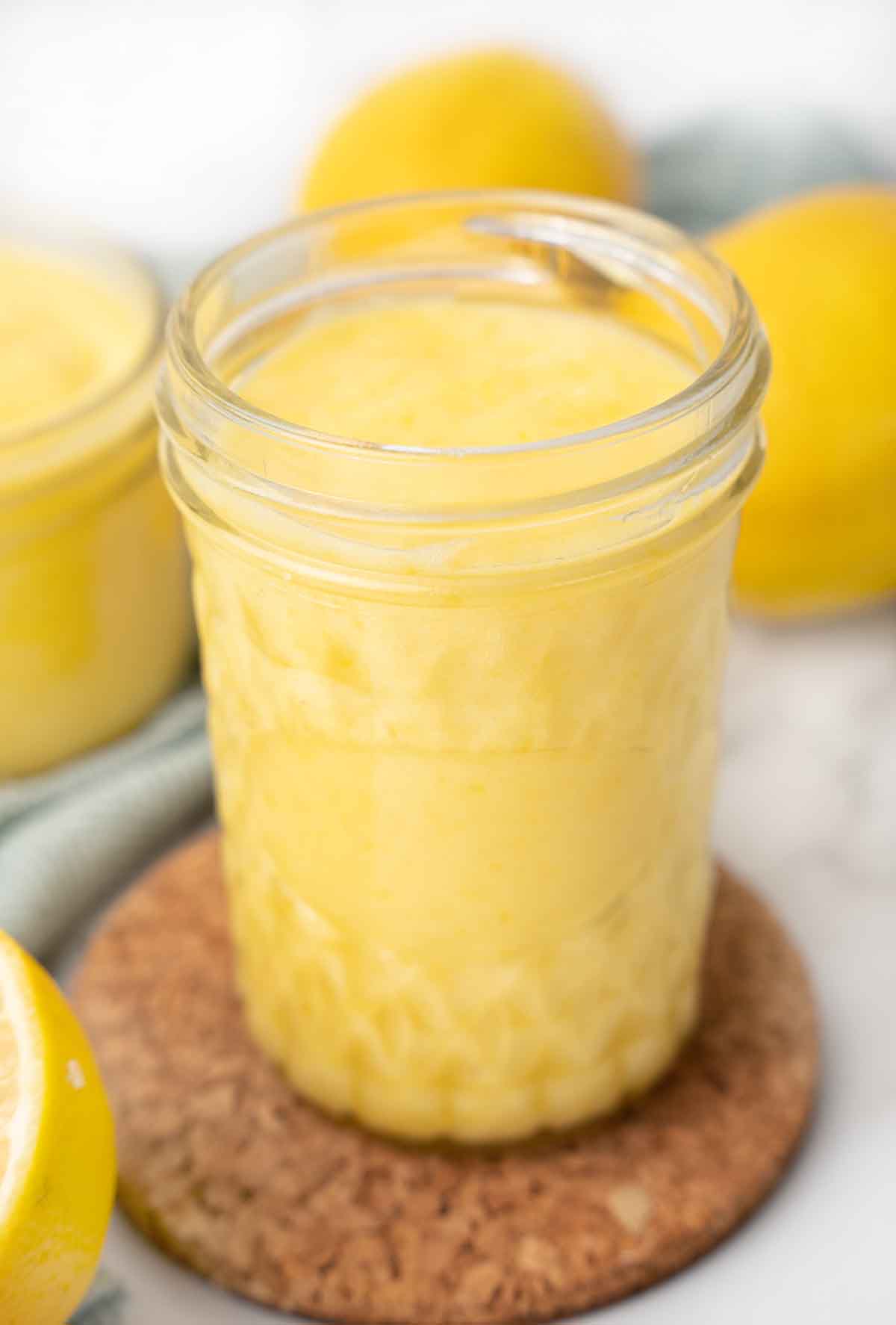 jar of lemon curd, with lemons and another jar in the background.