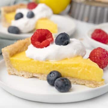 slice of lemon tart with whipped cream and berries on a white plate.