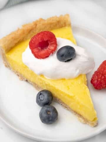 slice of lemon tart with whipped cream and berries on a white plate.