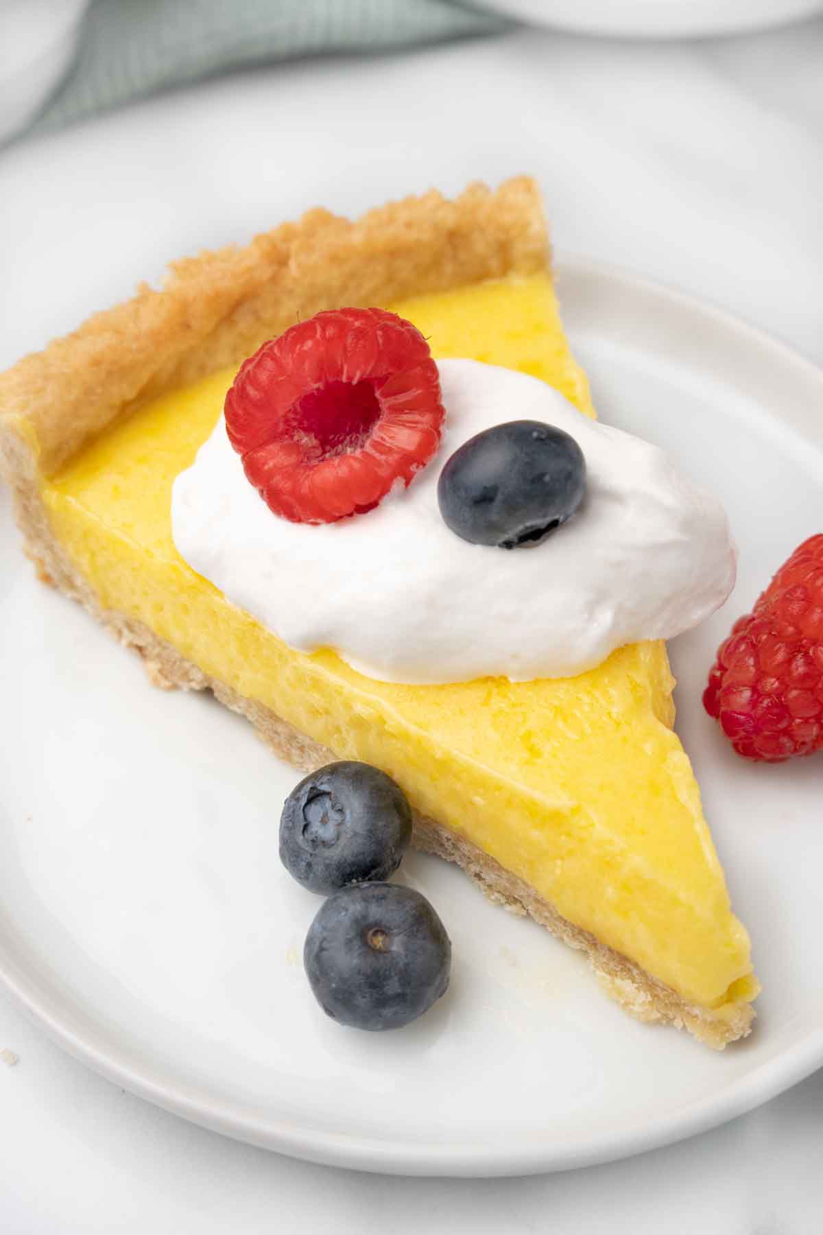 slice of lemon tart with whipped cream and berries on a white plate.