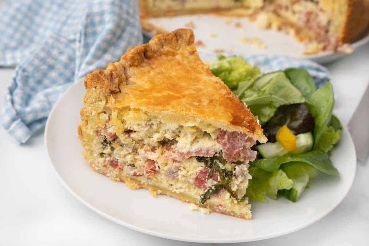 Slice of Pizza Rustica (Italian Easter Pie) on a white plate with salad.