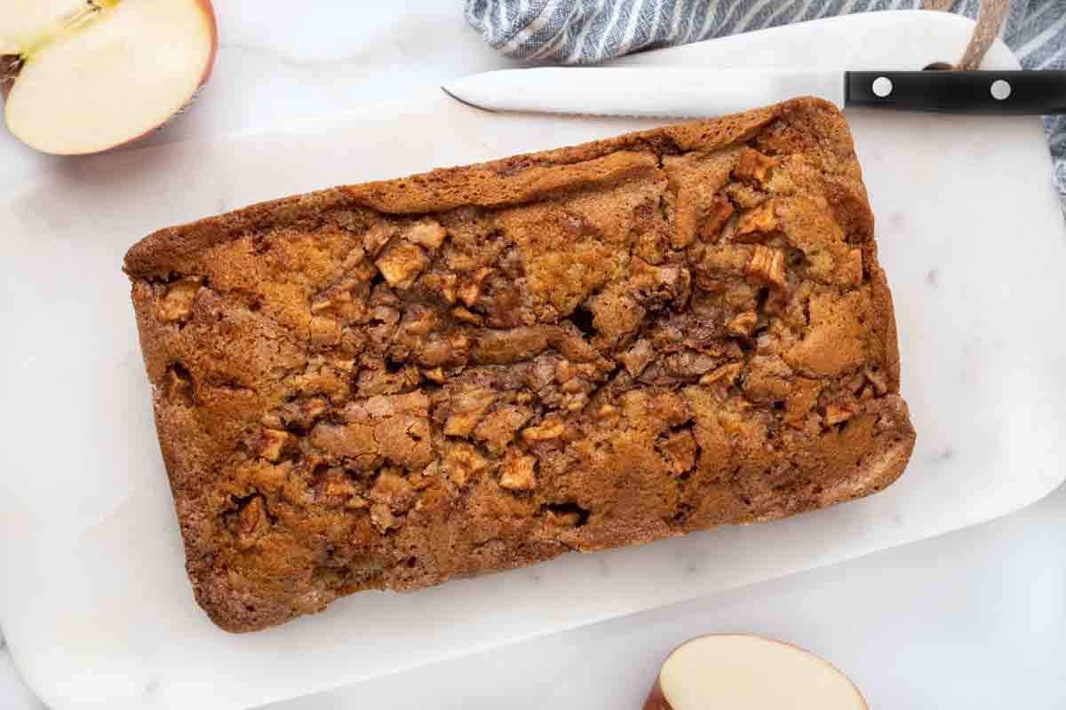 Whole loaf of apple bread on a white cutting board.