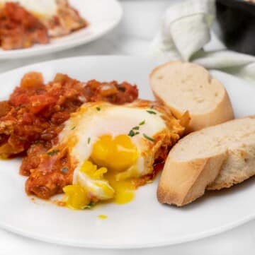 portion of eggs in purgatory on a white plate with bread slices.