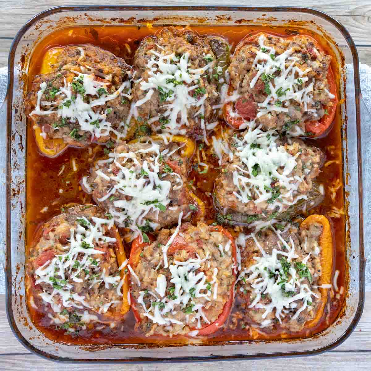 Baked stuffed peppers with sauce in a glass baking dish.
