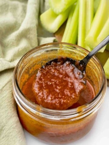 Nashville hot sauce in a glass jar with a black spoon.