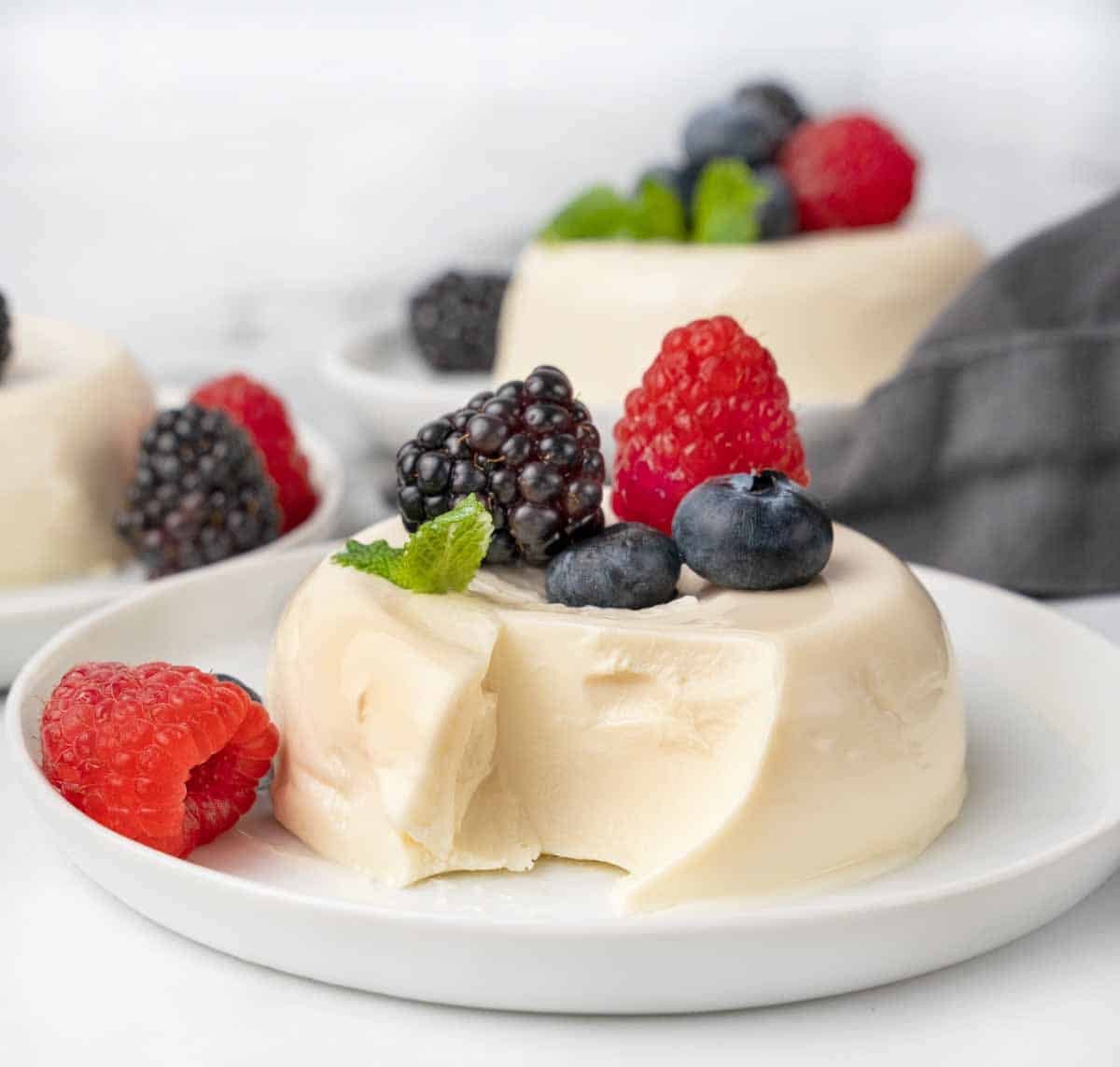 Panna cotta with a spoonful taken out on white plate with berries.