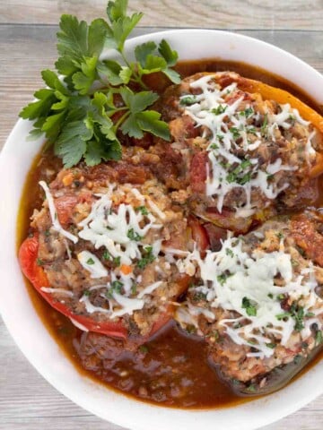 Three stuffed peppers in a white bowl with sauce.