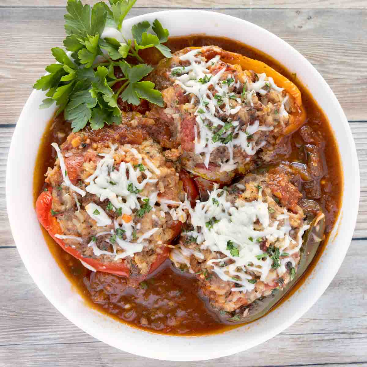 Three stuffed peppers in a white bowl with sauce.