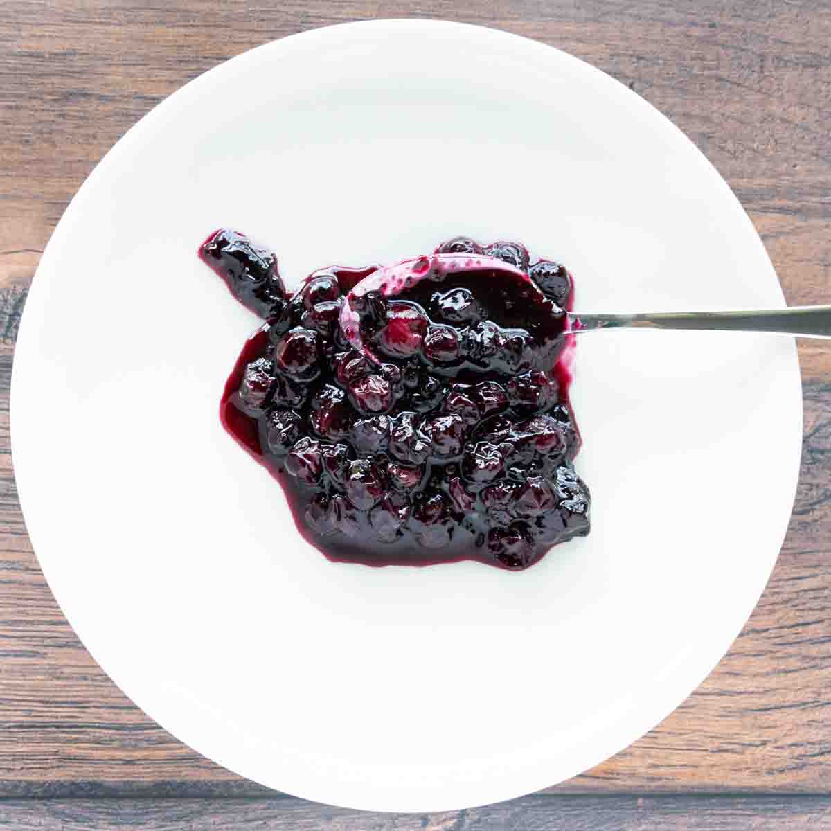 Blueberry compote with a spoon on a white plate.