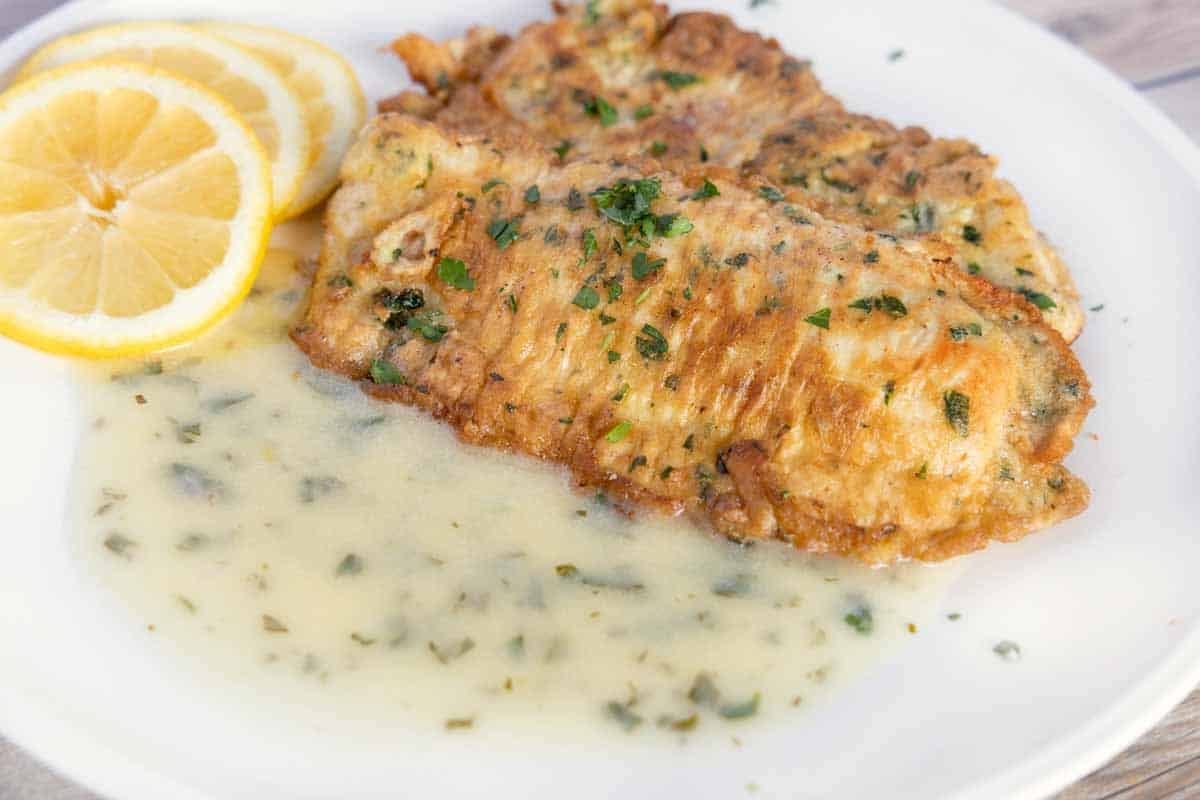 flounder francaise with lemon butter sauce and lemon circles on a white plate