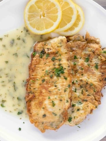 flounder francaise with lemon butter sauce and lemon circles on a white plate