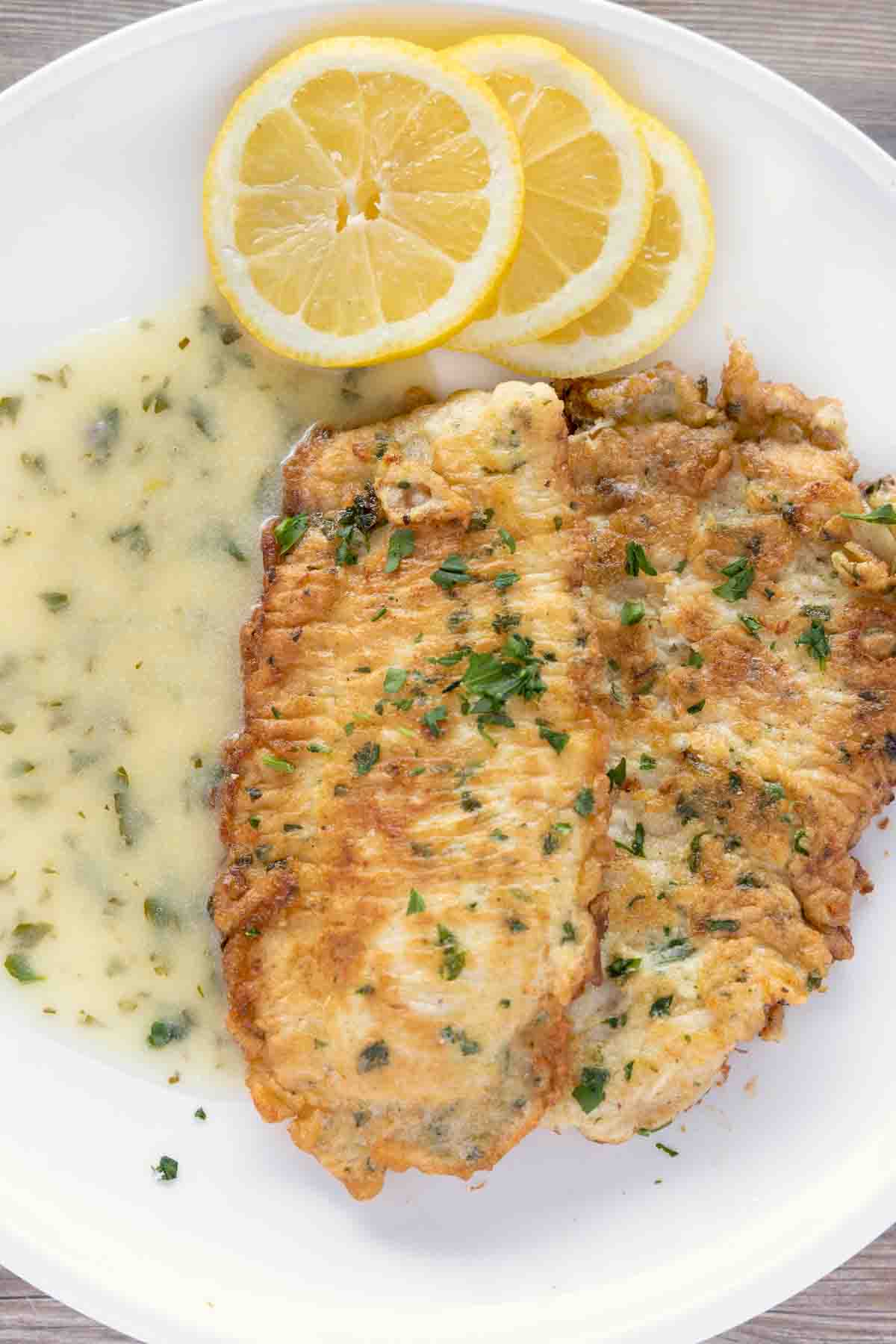 flounder francaise with lemon butter sauce and lemon circles on a white plate