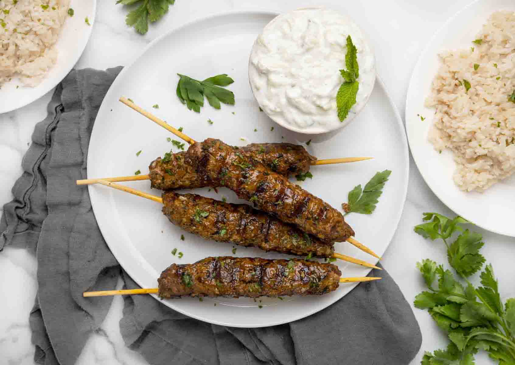 Beef Kofta Kebabs with a bowl of tzatziki sauce on a white plate.