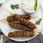 Beef kofta kebabs on a white plate with bowl of tzatziki sauce