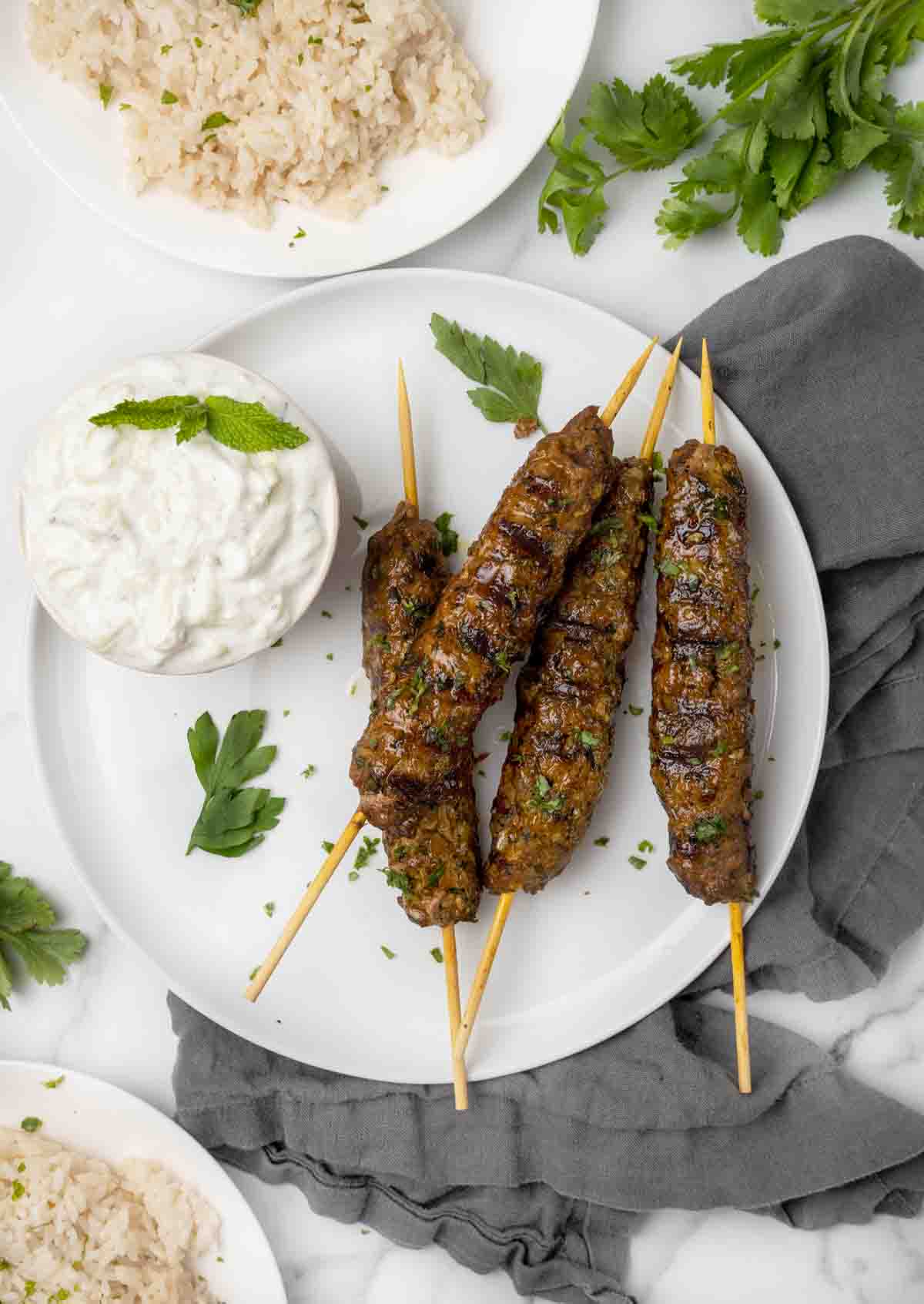Kafta Kababs  with a bowl of tzatziki sauce on a white plate.