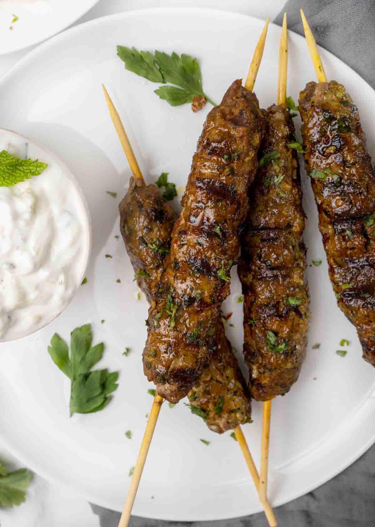 Beef Kofta Kebabs with a bowl of tzatziki sauce on a white plate.