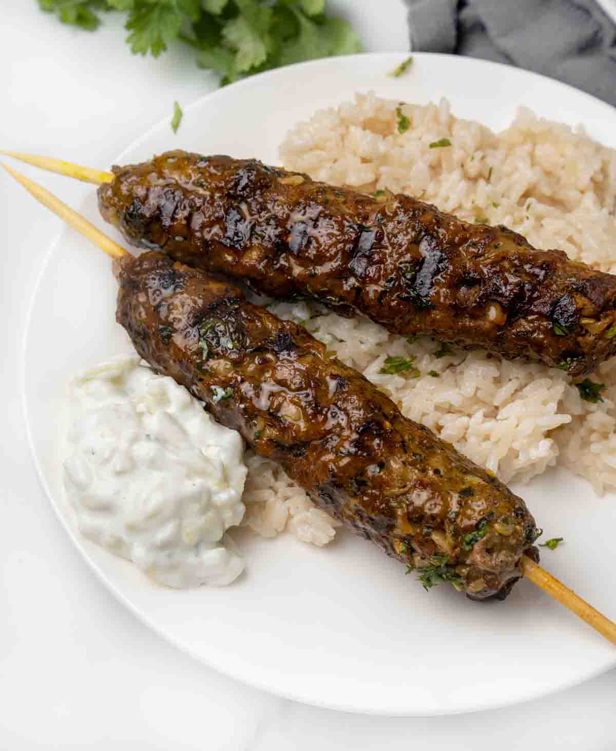 Beef Kofta Kebabs on rice with a side of tzatziki sauce on a white plate.