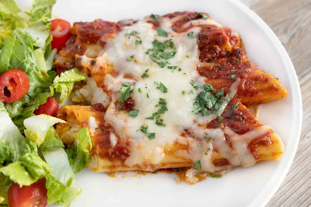 baked cheese manicotti with side salad on a white plate.