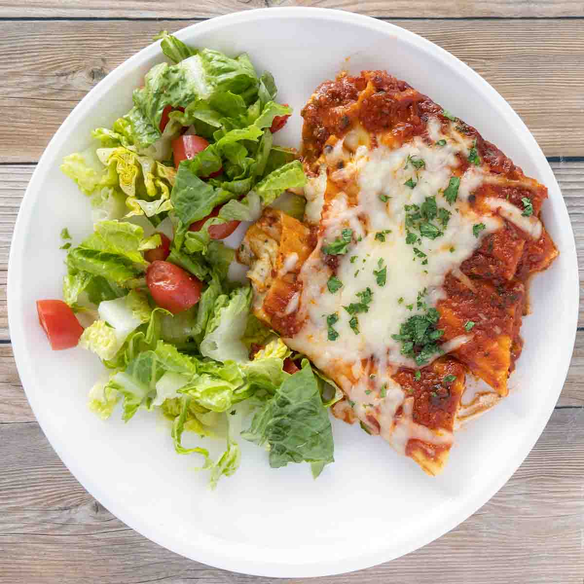baked manicotti with side salad on a white plate.