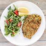 Veal Milanese on white plate with arugula salad and lemon wedges.