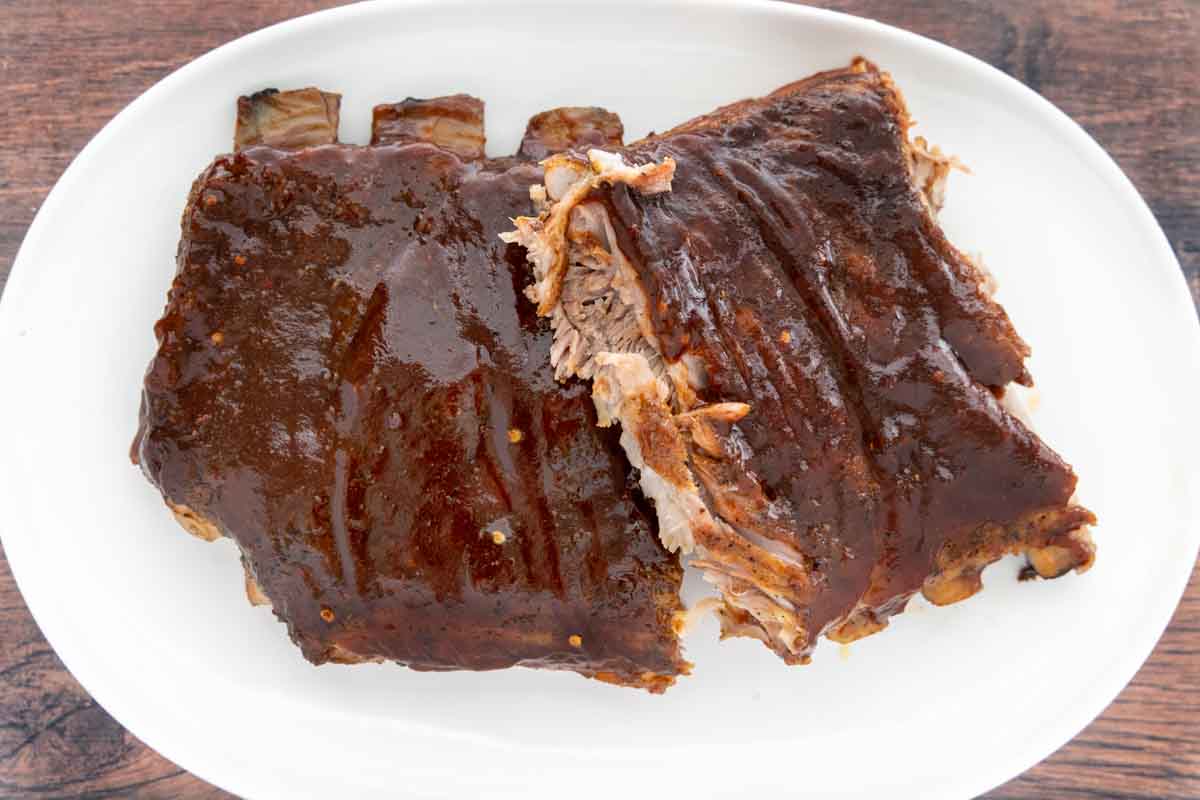 smoked St. Louis style ribs with bbq sauce cut into sections on a white platter.