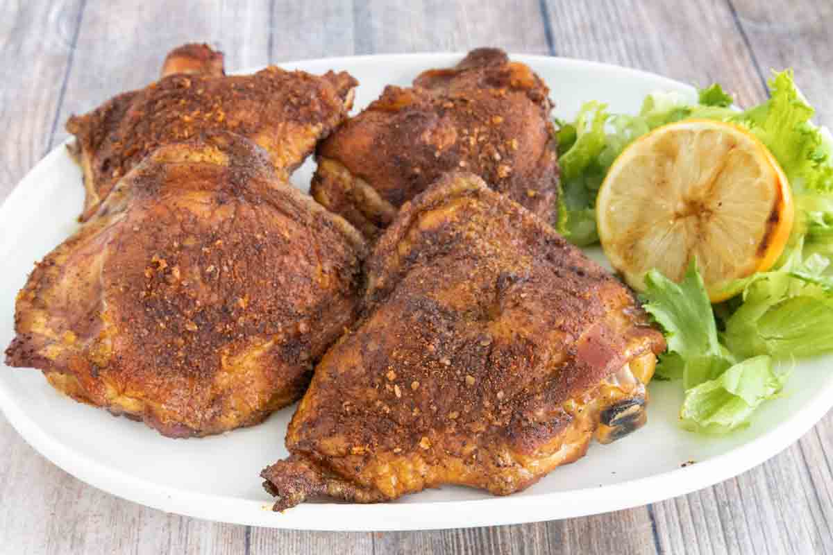 Smoked Chicken Thighs on a white platter with lettuce and smoked lemon half.