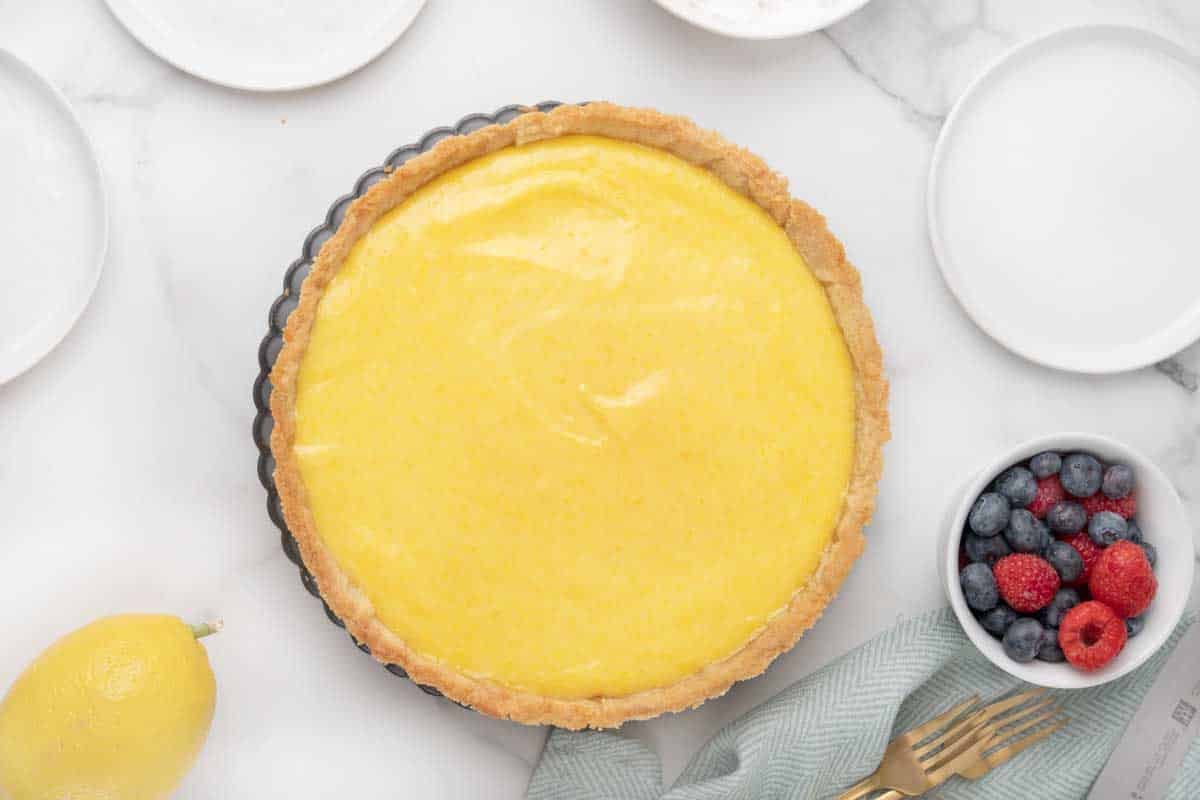 whole lemon tart with a bowl of berries.