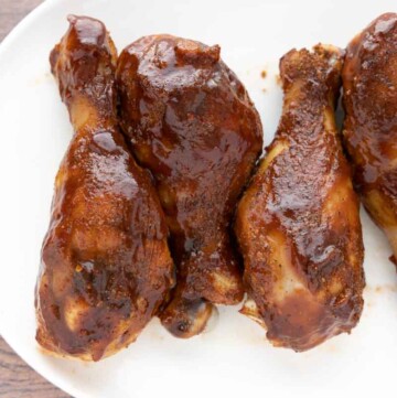 smoked chicken legs with barbecue sauce on a white platter.