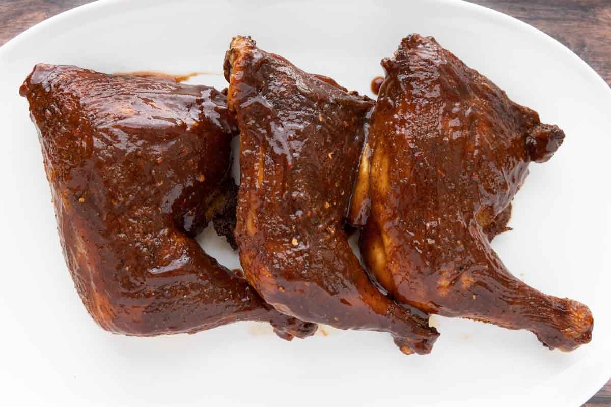 smoked chicken leg quarters with barbecue sauce on a white platter.