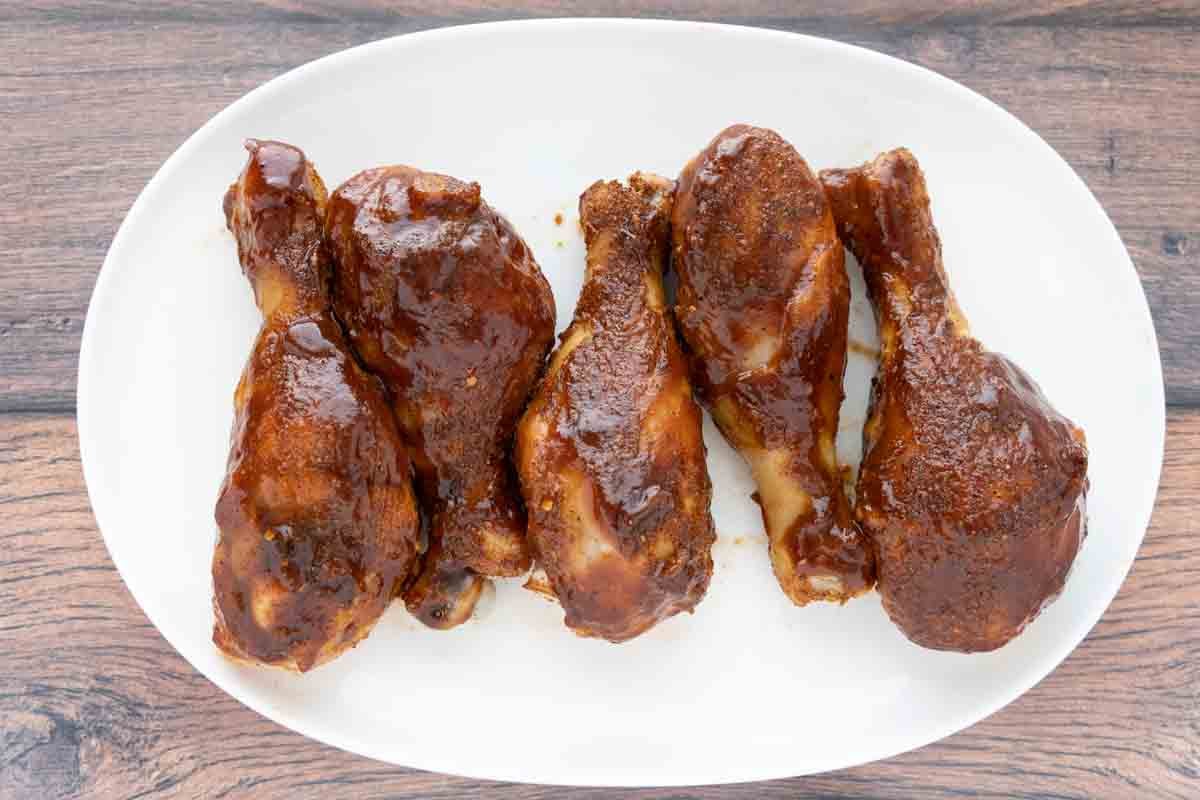 smoked chicken legs with barbecue sauce on a white platter.