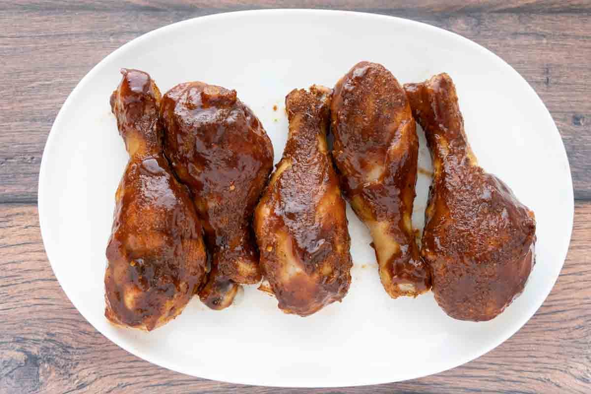 Finished chicken legs with barbecue sauce on a white platter.