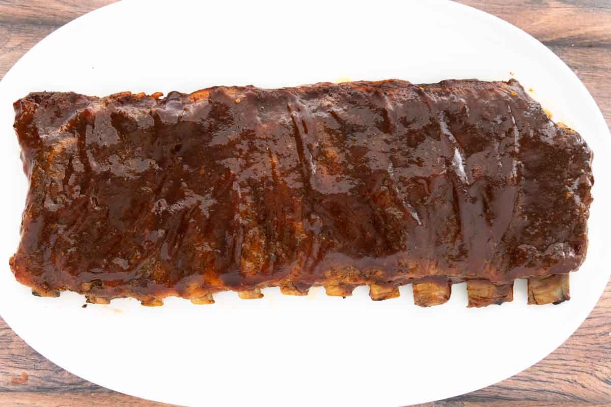 smoked St. Louis style ribs with bbq sauce cut into sections on a white platter.