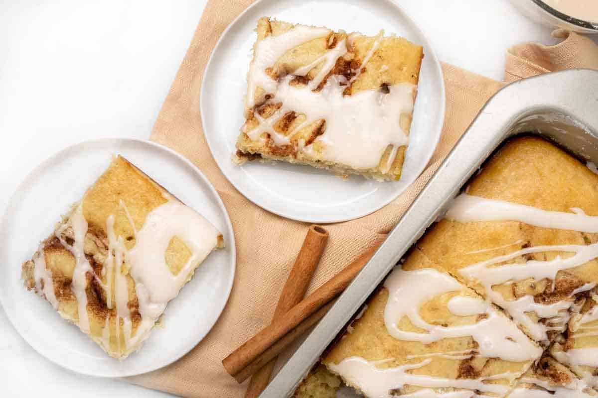 slices of cinnamon roll cake on white plates next to pan with cake.