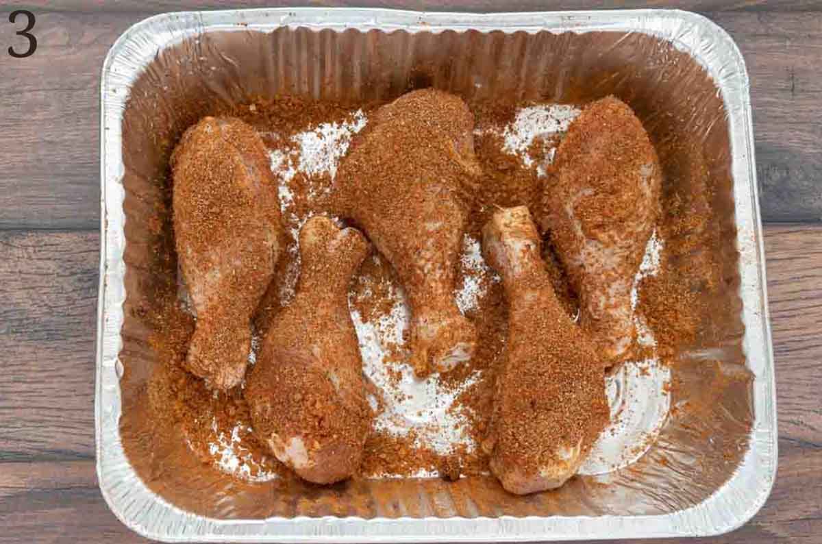 raw drumsticks with seasoning in a foil pan.