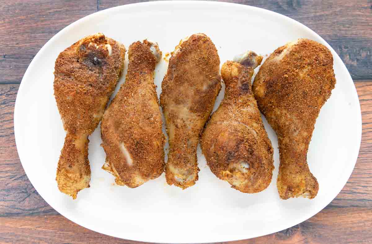 Seasoned chicken legs on a white platter.